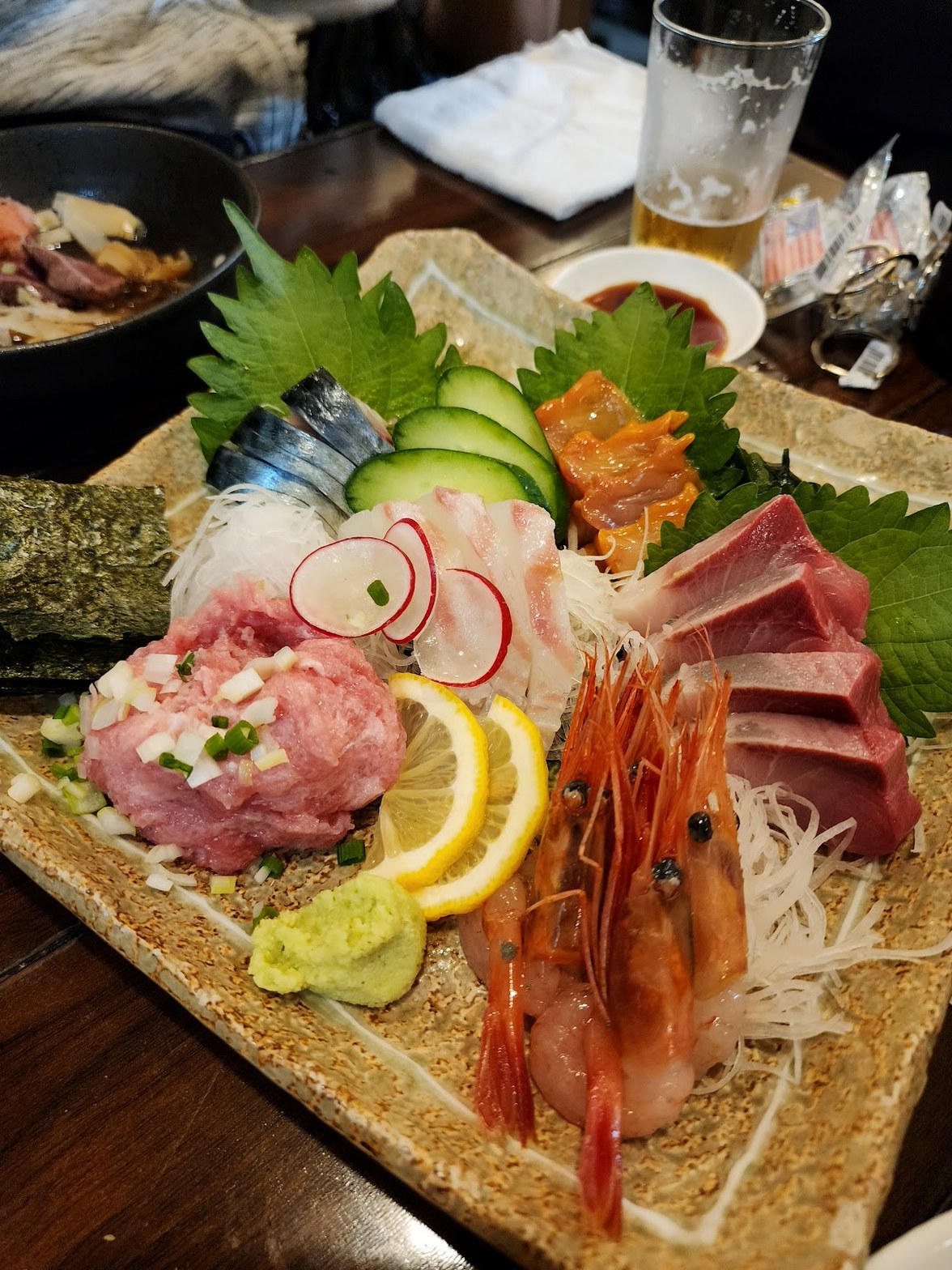 石目皿に盛られた刺し盛り。本鮪・鰤・鯵・烏賊・海老・中落ちなど多種の魚介と大葉、レモン、わさびが並ぶ